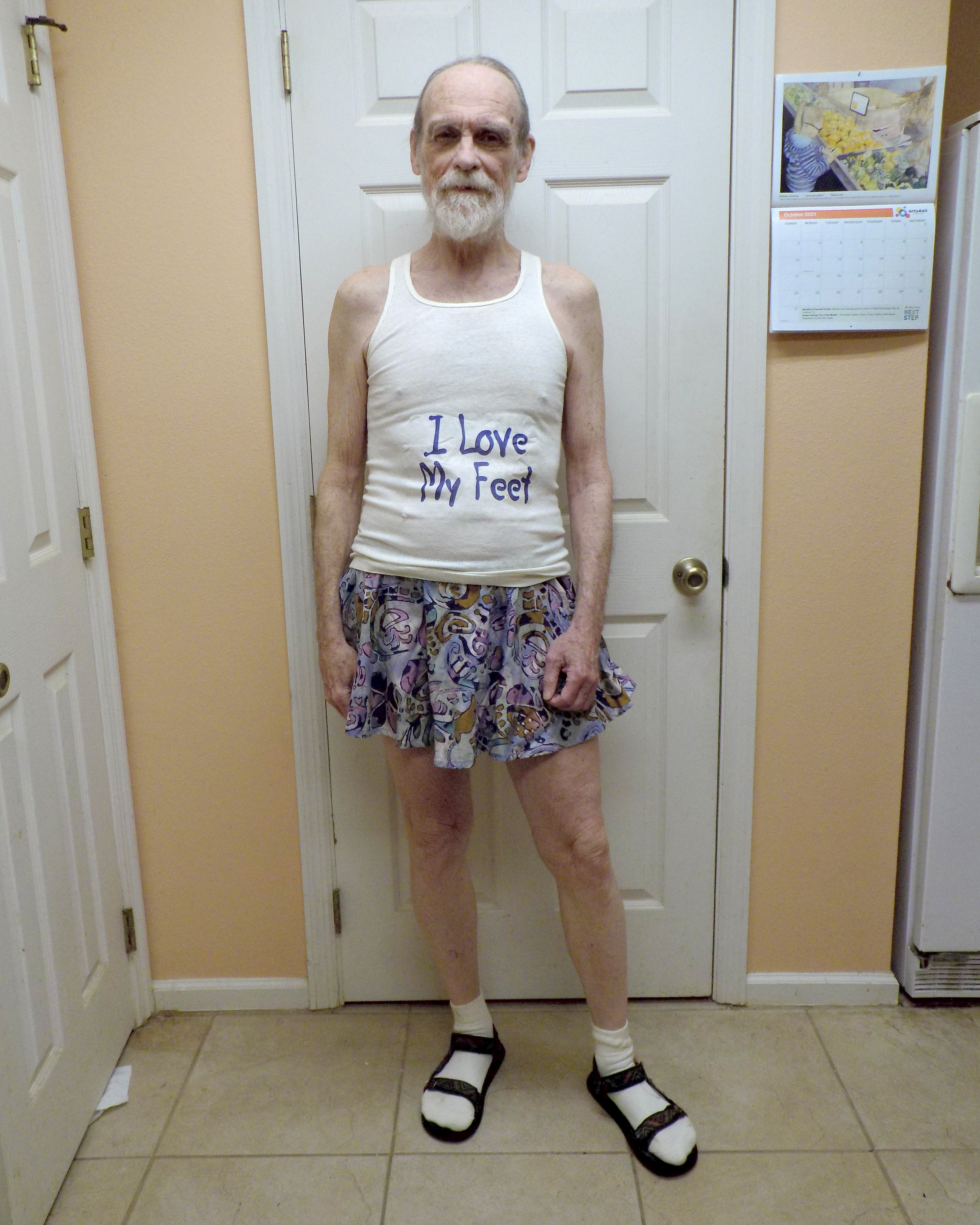 Wearing a tank top that says 'I Love My Feet' and men's skirt with socks and sandals
